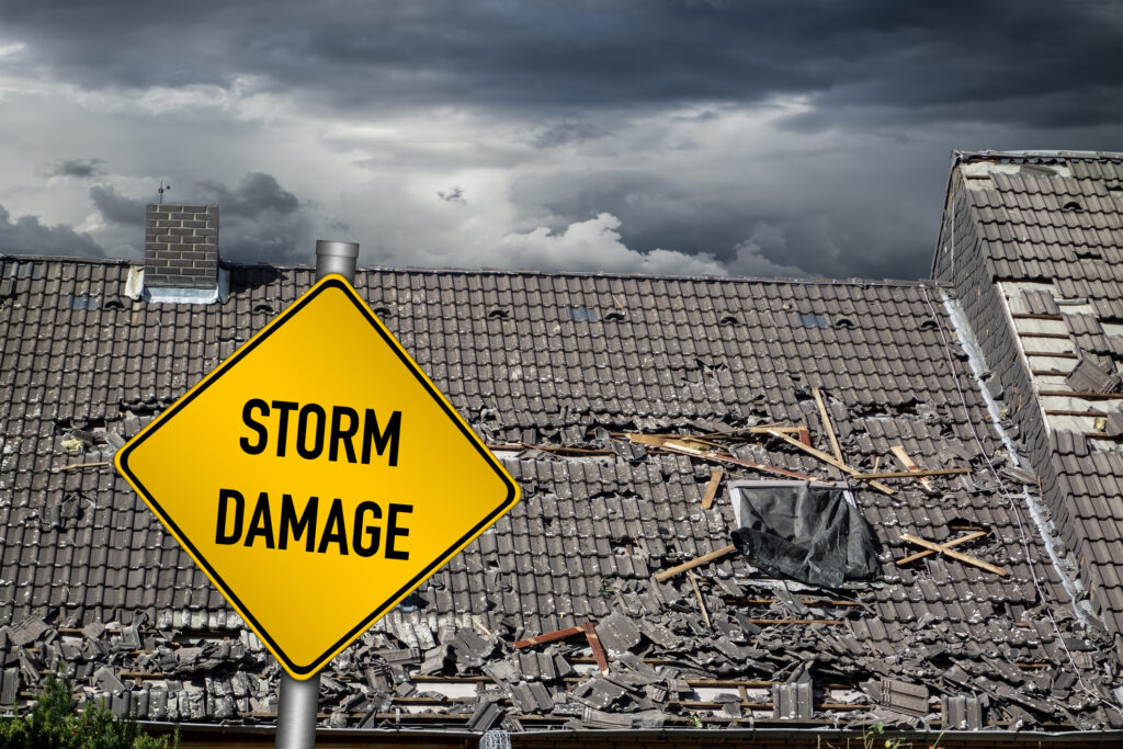 yellow damage warning sign in front of roof of house damaged by a bad storm or natural disaster